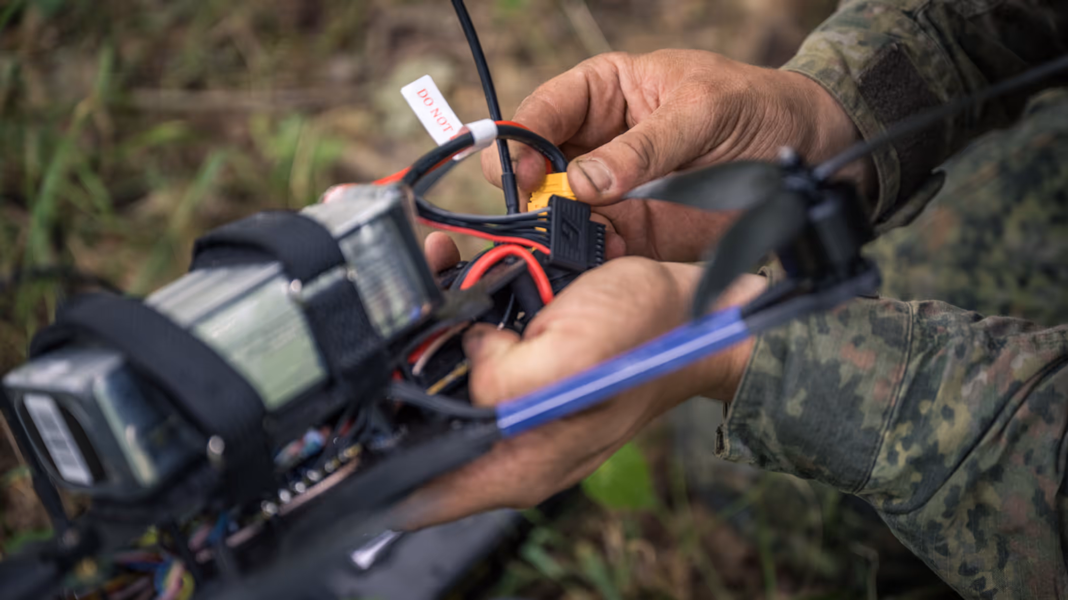 Een drone-operator zit met zijn handen aan een drone. 
