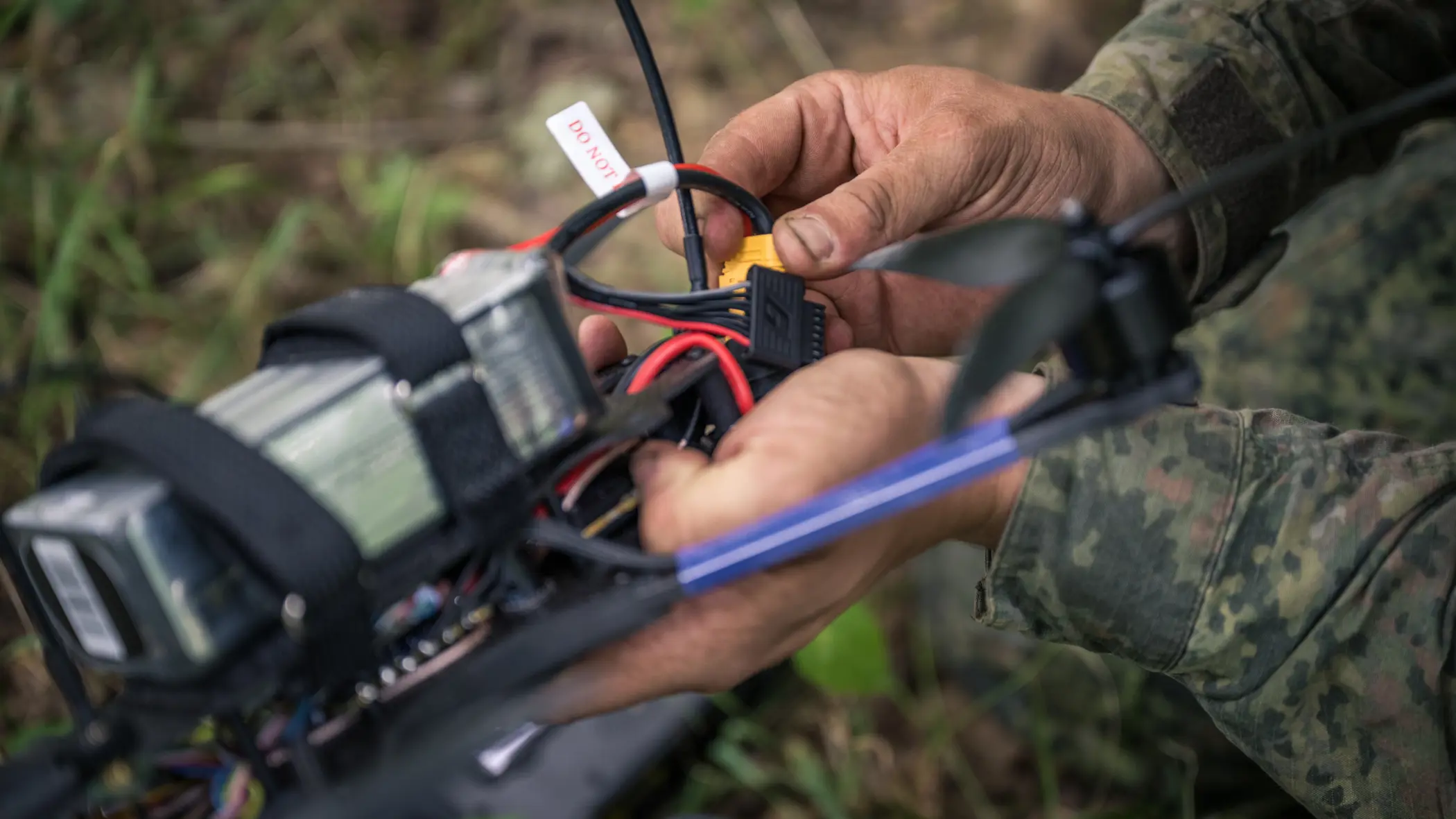 Een drone-operator zit met zijn handen aan een drone. 