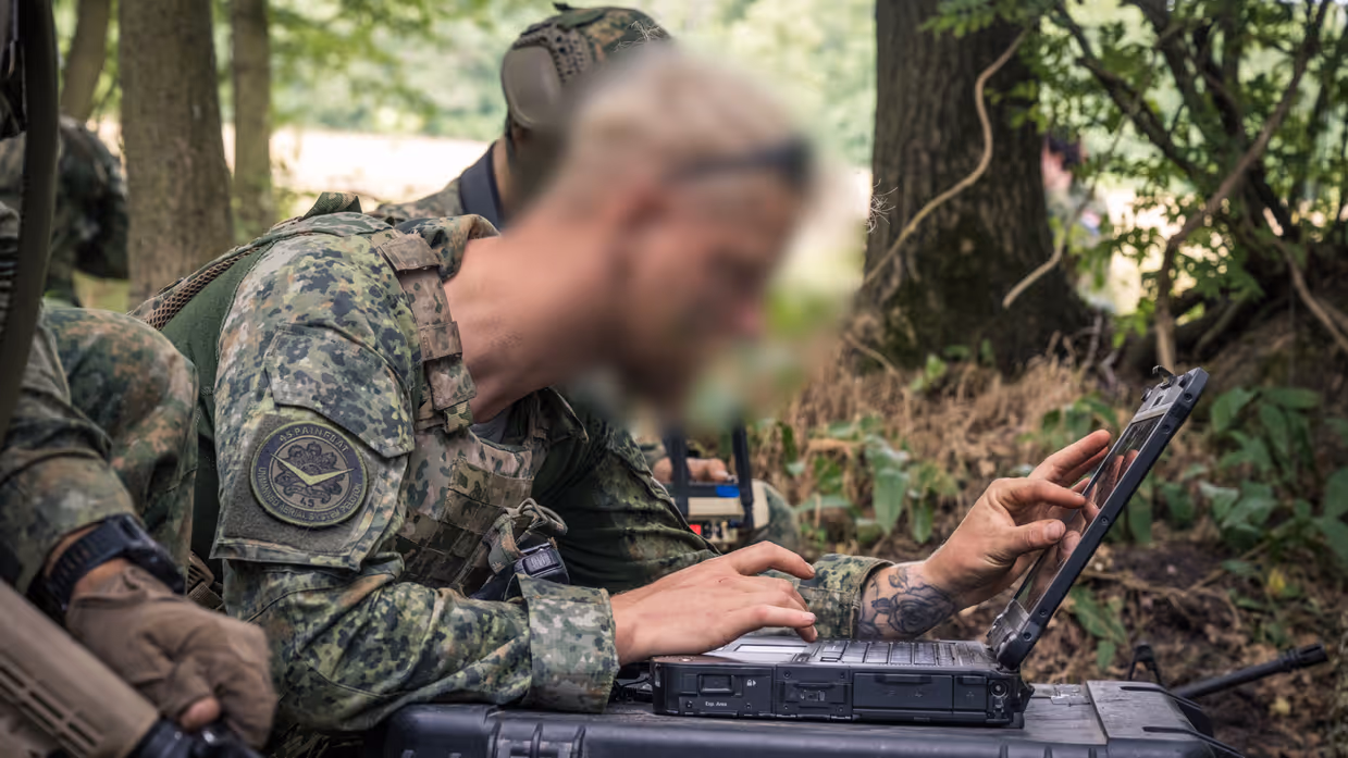 Een militair tuurt in het veld naar het scherm van een tablet.