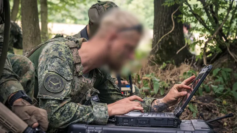 Een militair tuurt in het veld naar het scherm van een tablet.