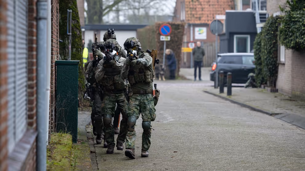 Militairen lopen met getrokken wapen door een straat.
