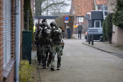 Militairen lopen met getrokken wapen door een straat.