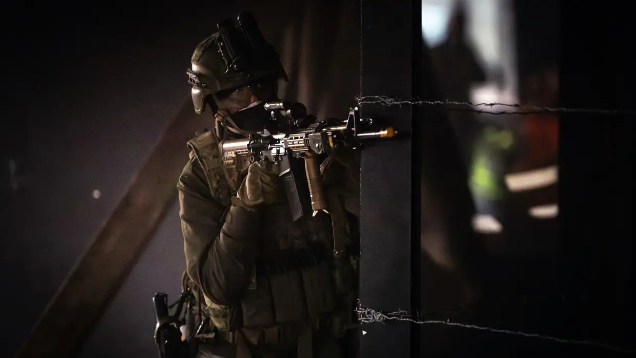 Militair in half duister richt geweer om de hoek.