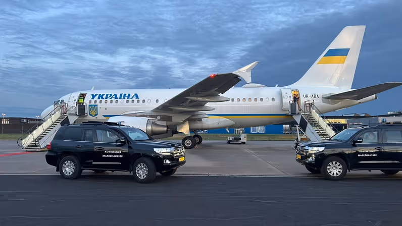 Regeringstoestel van de Oekraïense president met voertuigen van de Marechaussee ervoor.