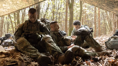 Militairen rusten en bereiden zich voor onder een gecamoufleerd schuilzeil.