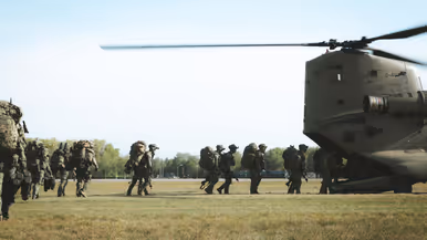 Militairen met zware bepakking lopen richting een Chinook-helikopter.