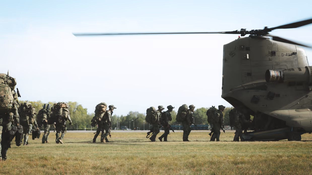 Militairen met zware bepakking lopen richting een Chinook-helikopter.