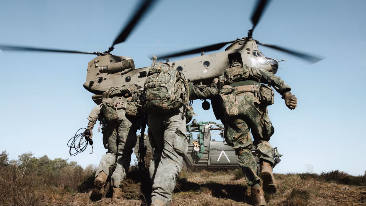 Militairen rennen met zware bepakking richting een Chinook-helikopter tijdens een luchtmobiele operatie.
