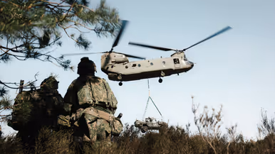 Militairen met zware bepakking lopen richting een Chinook-helikopter.