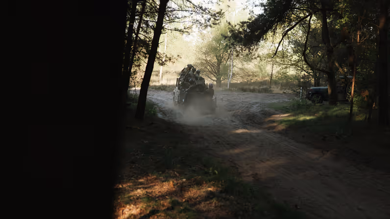 Militairen verplaatsen zich met een voertuig over een zandpad door het bos tijdens oefening Versatile Guard.