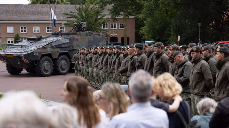 Groep militairen staat op plein met publiek aan de zijkant.
