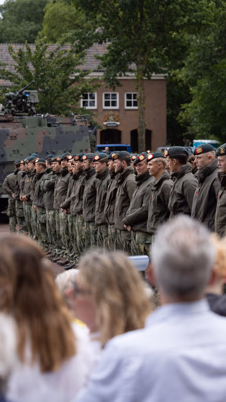 Groep militairen staat op plein met publiek aan de zijkant.