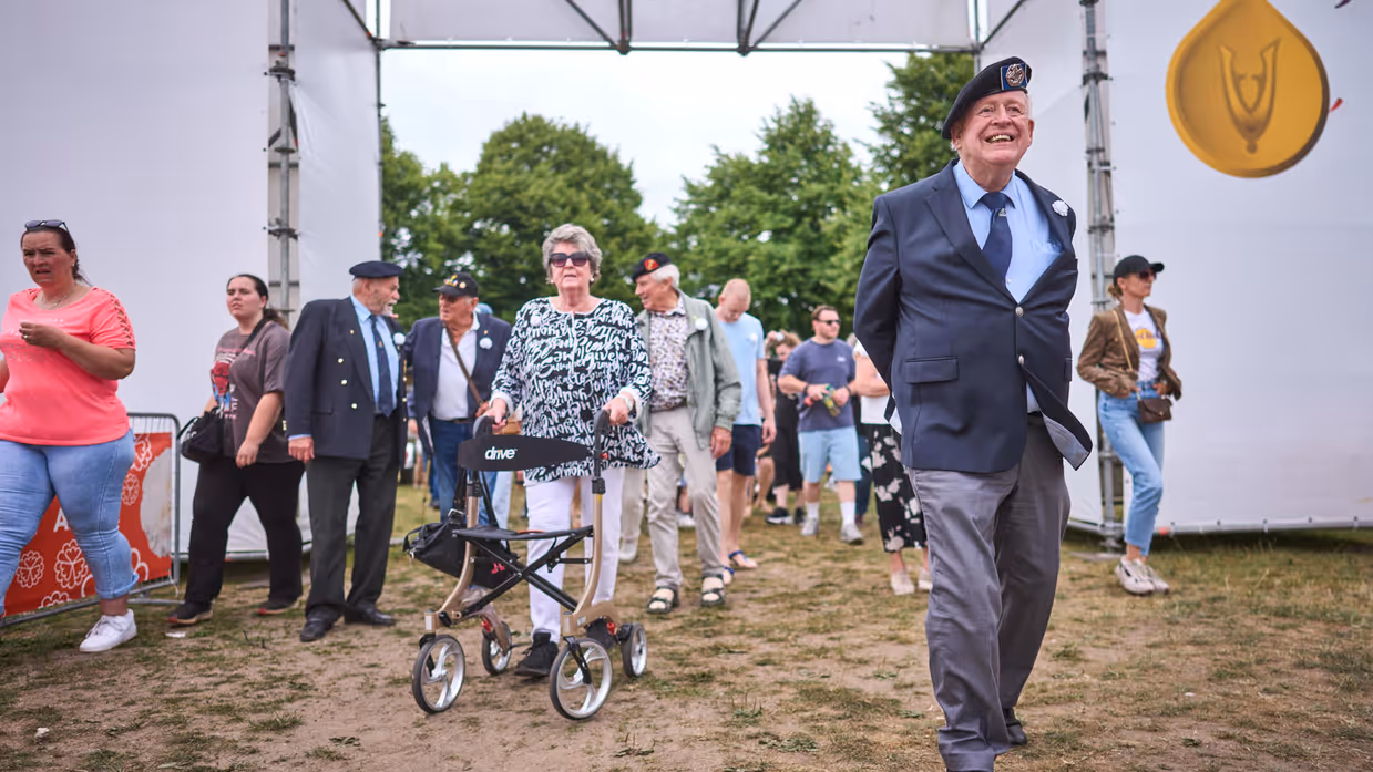 Een veteraan loopt lachend door de toegangspoort van het evenement.