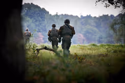 Militairen van achteren gezien lopen door een landschap.