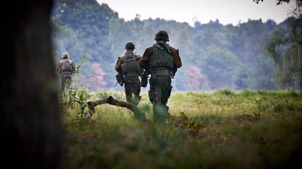 Militairen van achteren gezien lopen door een landschap.