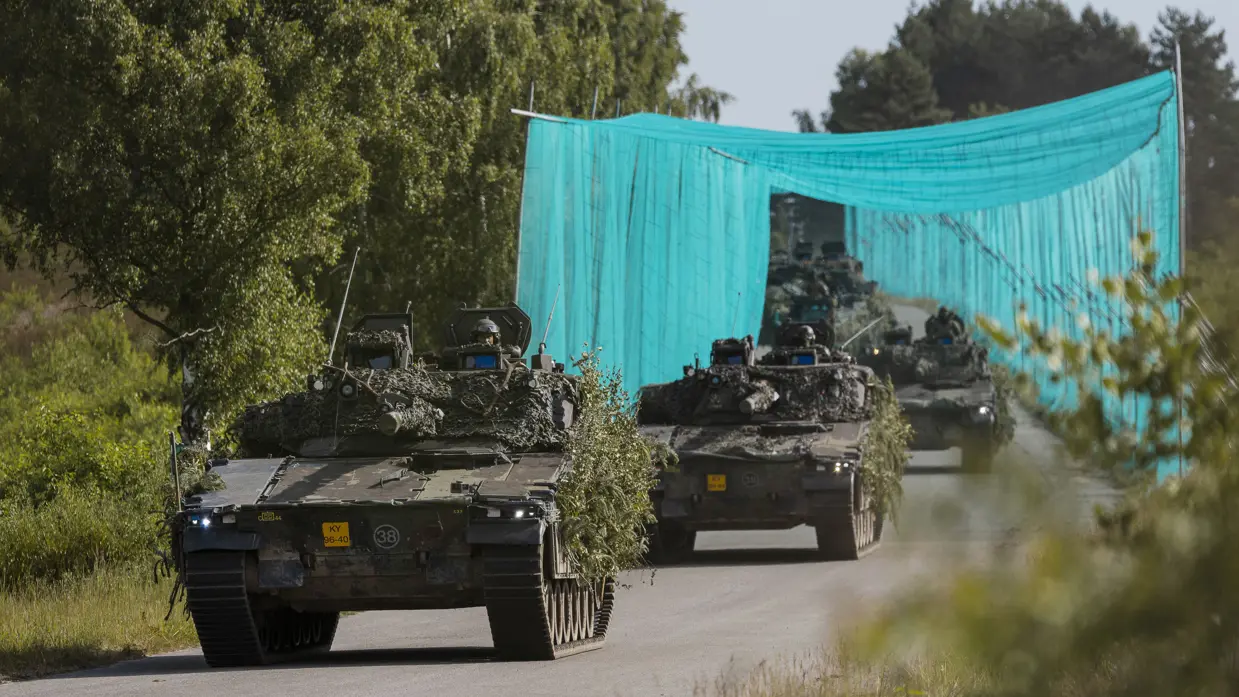 Militaire voertuigen rijden onder een antidronenet door. 