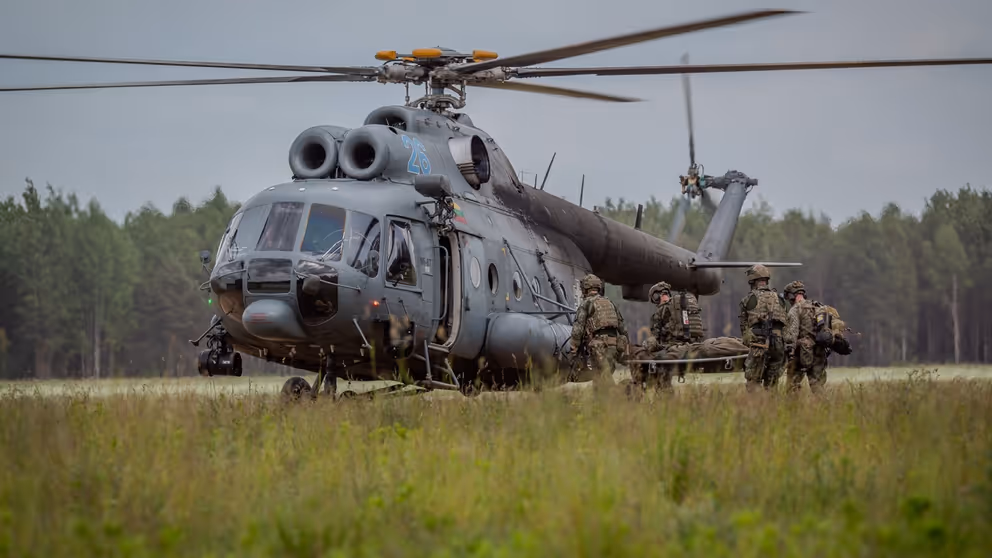 Militairen brengen een militair op een brancard naar een helikopter.