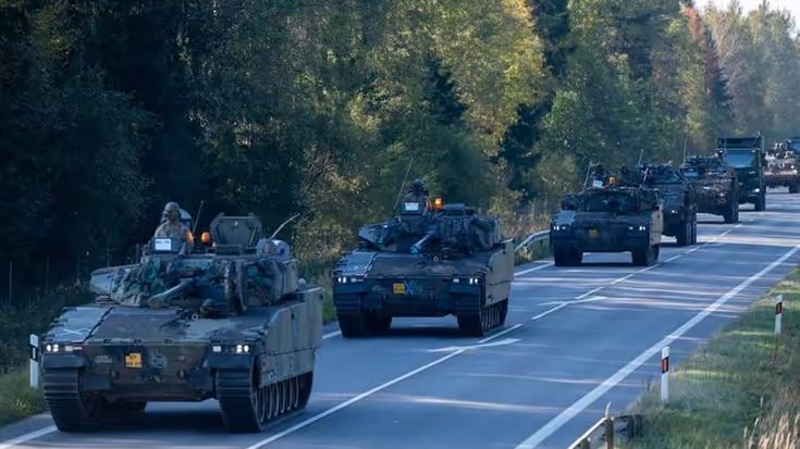 Militaire voertuigen in kolonne op een Litouwse weg.