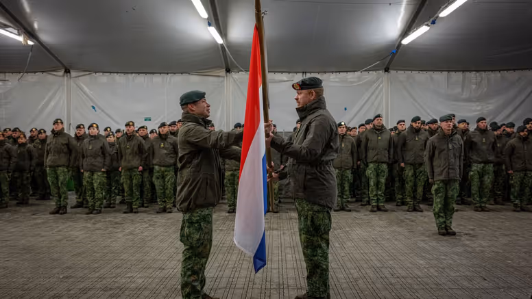 Alt-tekst: 2 militairen staan tegenover elkaar en houden Nederlandse vlag vast. 