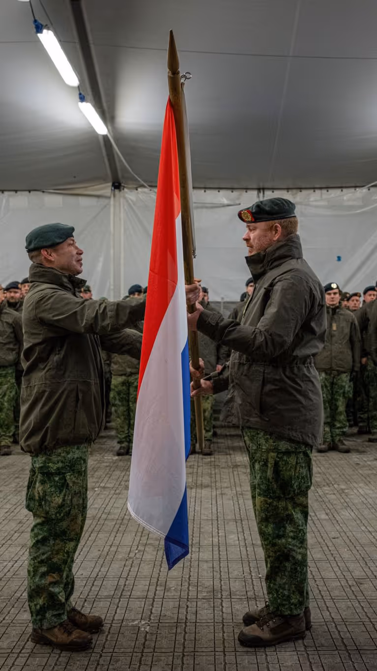 Alt-tekst: 2 militairen staan tegenover elkaar en houden Nederlandse vlag vast. 