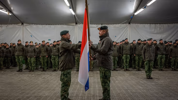 Twee militairen staan tegenover elkaar met een vlag tussen hen in. Op de achtergrond nog meer militairen. 