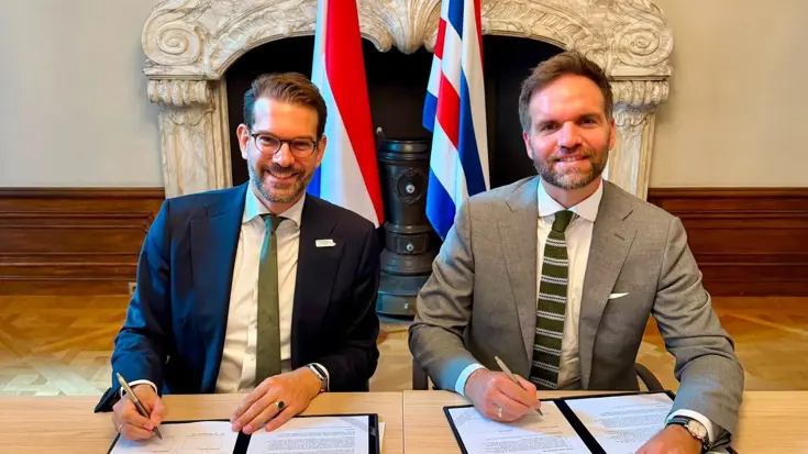 Twee mannen zitten achter een tafel en ondertekenen een formulier.
