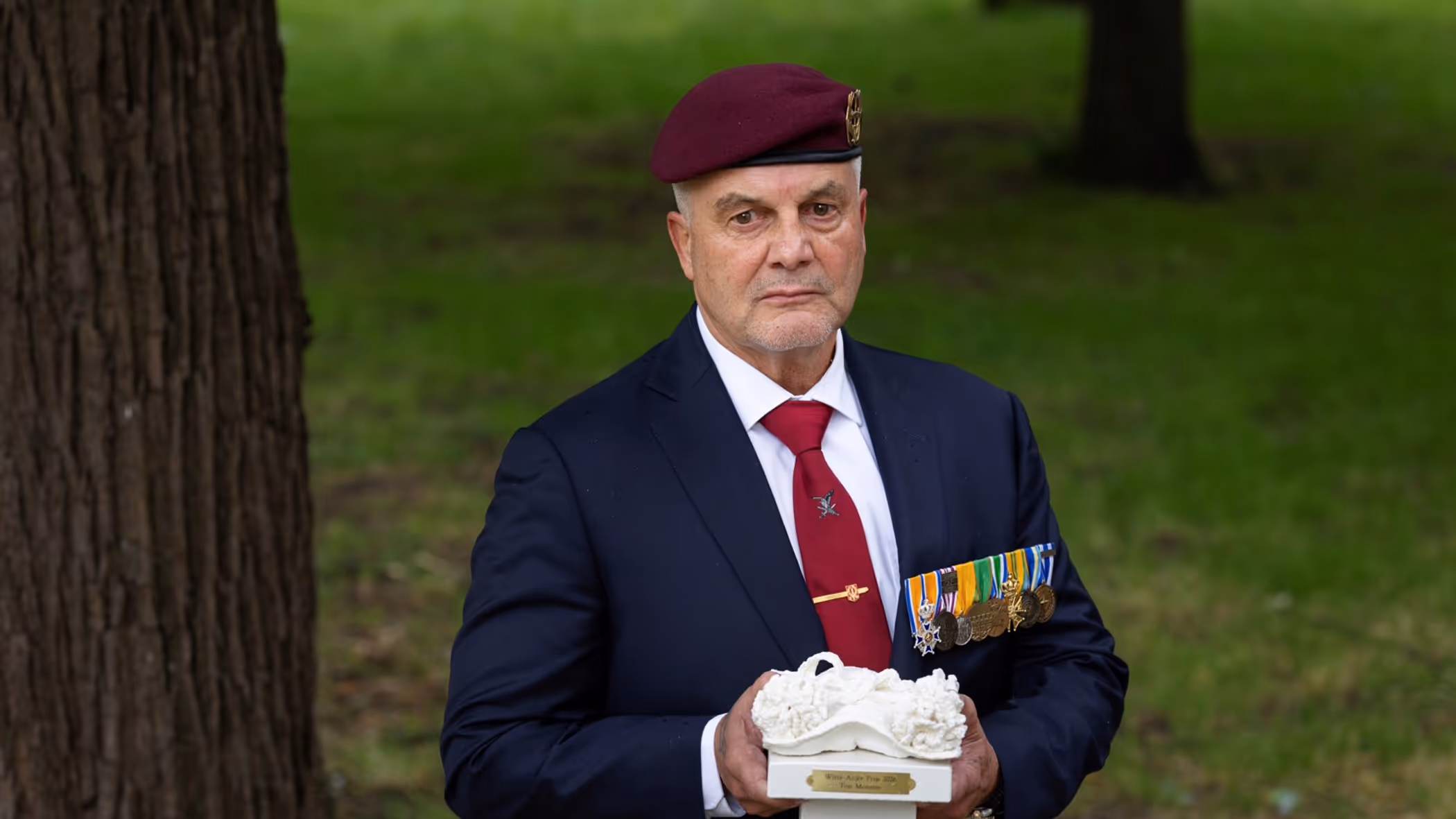 Veteraan houdt een beeldje van een witte anjer in zijn handen. 