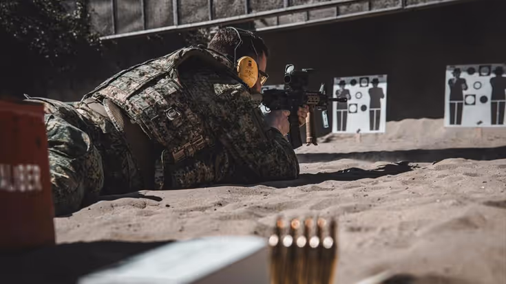 Militair ligt plat op de grond tijdens schietoefening en richt wapen op doel.
