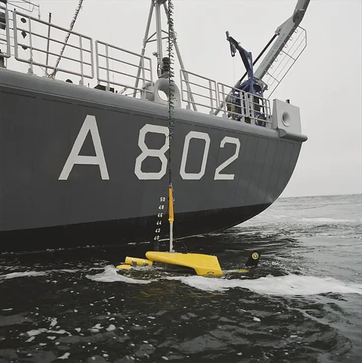 Close up van de zijkant van Zr.Ms. Snellius. In het water drijft een meetinstrument dat door de Snellius te water is gelaten.