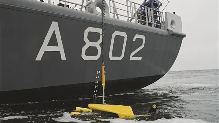 Close up van de zijkant van Zr.Ms. Snellius. In het water drijft een meetinstrument dat door de Snellius te water is gelaten.