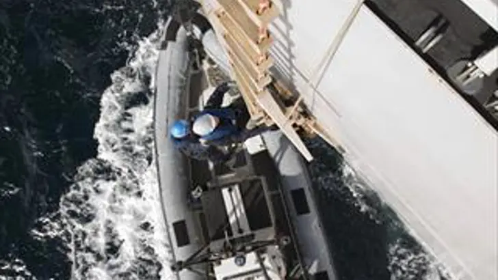 Een persoon klimt uit een RHIB met een ladder omhoog op een schip.