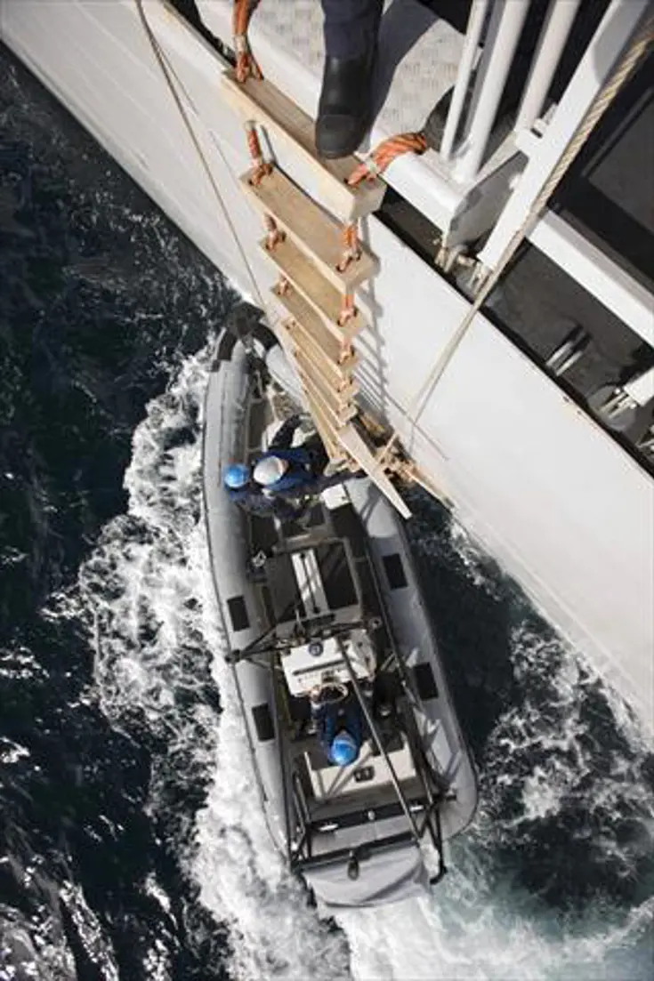 Een persoon klimt uit een RHIB met een ladder omhoog op een schip.